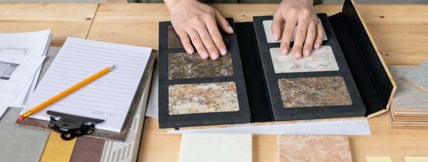 Hands of designer on samples of marble tile surrounded by wallpaper patterns during work over new project or order of client